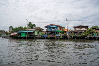 Chao Phraya nehrinin uzun kuyruklu ahşap botları ve Bangkok Tayland Asya 'daki konut binaları olan klong veya nehir kanalı.