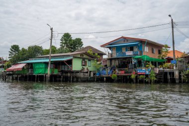 Chao Phraya nehrinin uzun kuyruklu ahşap botları ve Bangkok Tayland Asya 'daki konut binaları olan klong veya nehir kanalı.