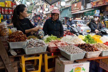 Vietnamlı bir kadın, Vietnam 'da, Hanoi' nin eski mahallesindeki bir sokak dükkanında motosikletli bir müşterisiyle tezgahtar olarak çalışıyor..