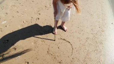 Kız çocuğu kumsalda sopayla çiziyor ve eğleniyor. Yüksek kalite 4k görüntü