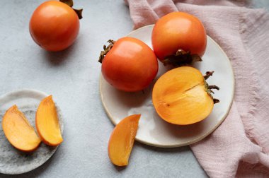 Olgun Sharon hurmaları ikiye bölünmüş ve gri arkaplanda tekstil içeren bir tabakta dilimlere bölünmüş..