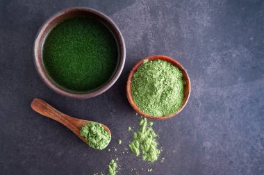 Ahşap arka planda bir kasede yeşil arpa tozu. Kibrit ya da klorella içeceği..