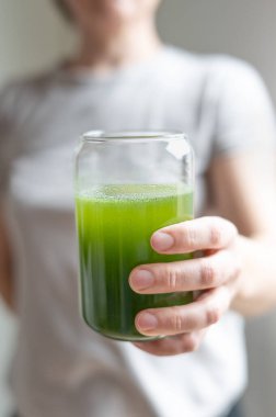 Genç arpa ve klorella spirulina tozundan ya da kibrit çayından bardakla su içen kadın, sağlıklı yeşil meyve suyu..