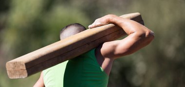 Yarış testinde tahta kütük taşıyan bir adam. Çamur yarışçıları, aşırı engelli koşucular