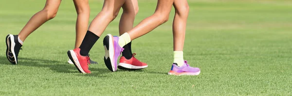 三个女运动员跑步 脚踏在草地上 女性和男性健康阳光慢跑锻炼 体育运动员积极的生活方式的概念 日落时跑腿在草地上跑的运动员 — 图库照片
