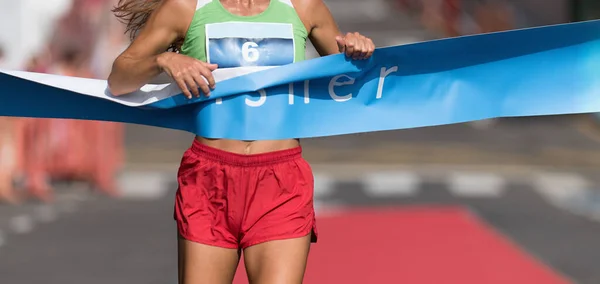 フィニッシュラインに向かって走っている女性 女性ランナーは市内の屋外レースに勝つ 勝者としてフィニッシュラインを通過 — ストック写真