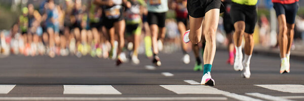 Марафонцы бегут по городской дороге, большая группа бегунов, бегуны на ногах крупным планом, бегуны на асфальте, легкая атлетика