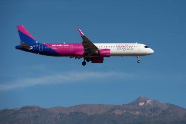 Tenerife, İspanya 20 Ekim 2024. Airbus A321-271NX Wizz Air Airlines mavi gökyüzünde uçuyor. Tenerife Havaalanına iniyor. Arka planda El Teide volkanı