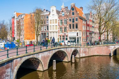 AMSTERDAM, HOLLLAND - 17 Nisan 2023: Amsterdam, Hollanda 'da özenle hazırlanmış kanal sistemi, dar evleri ve şehir çevresinde sayısız bisiklet yolu bulunan bisiklet yollarıyla bilinen bir kanal manzarası