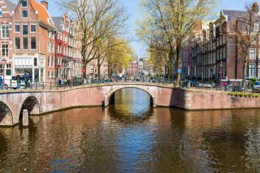 AMSTERDAM, HOLLLAND - 17 Nisan 2023: Amsterdam, Hollanda 'da özenle hazırlanmış kanal sistemi, dar evleri ve şehir çevresinde sayısız bisiklet yolu bulunan bisiklet yollarıyla bilinen bir kanal manzarası