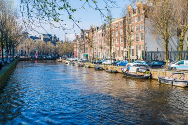 AMSTERDAM, HOLLLAND - 17 Nisan 2023: Amsterdam, Hollanda 'da özenle hazırlanmış kanal sistemi, dar evleri ve şehir çevresinde sayısız bisiklet yolu bulunan bisiklet yollarıyla bilinen bir kanal manzarası