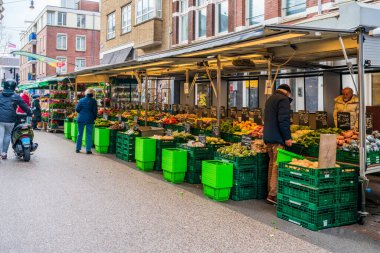 AMSTERDAM, HOLLAND - 18 Nisan 2023: Müşteriler Amsterdam Katestraat yerel sokak gıda pazarından taze ürün satın alıyorlar.