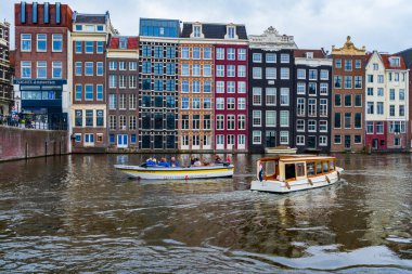 AMSTERDAM, HOLLAND - 17 Nisan 2023: Teknelerle turlar Hollanda 'nın başkentinde ayrıntılı kanal sistemi ve geniş cepheli geleneksel dar evleri ile bilinen kanallar boyunca bir yolculuğa çıkarlar
