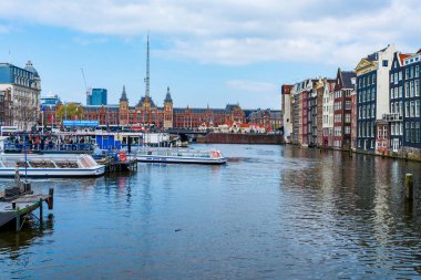 AMSTERDAM, HOLLAND - 18 Nisan 2023: Turistler, Hollanda 'nın başkentinde ayrıntılı kanal sistemi ve geniş cepheli geleneksel dar binalarıyla bilinen kanallar boyunca bir geziye çıkmak üzere teknelere biniyorlar