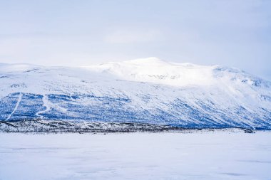 Frozen lake Tornetrask and snow covered mountains around Abisko, Sweden clipart
