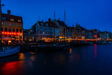 COPENHAGEN, DENMARK - 14 Nisan 2024: gece Nyhavn Kanalı. Eski evler, kafeler ve restoranların renkli cepheleriyle donatılmış Nyhavn Kanalı, Kopenhag 'ın en popüler turistik yerlerinden biri..