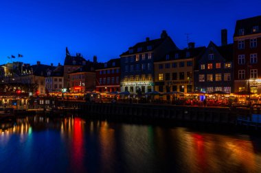 COPENHAGEN, DENMARK - 14 Nisan 2024: gece Nyhavn Kanalı. Eski evler, kafeler ve restoranların renkli cepheleriyle donatılmış Nyhavn Kanalı, Kopenhag 'ın en popüler turistik yerlerinden biri..