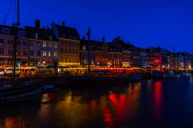 COPENHAGEN, DENMARK - 14 Nisan 2024: gece Nyhavn Kanalı. Eski evler, kafeler ve restoranların renkli cepheleriyle donatılmış Nyhavn Kanalı, Kopenhag 'ın en popüler turistik yerlerinden biri..