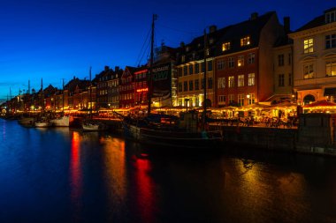 COPENHAGEN, DENMARK - 14 Nisan 2024: gece Nyhavn Kanalı. Eski evler, kafeler ve restoranların renkli cepheleriyle donatılmış Nyhavn Kanalı, Kopenhag 'ın en popüler turistik yerlerinden biri..