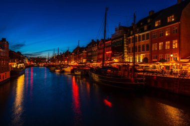 COPENHAGEN, DENMARK - 14 Nisan 2024: gece Nyhavn Kanalı. Eski evler, kafeler ve restoranların renkli cepheleriyle donatılmış Nyhavn Kanalı, Kopenhag 'ın en popüler turistik yerlerinden biri..