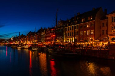 COPENHAGEN, DENMARK - 14 Nisan 2024: gece Nyhavn Kanalı. Eski evler, kafeler ve restoranların renkli cepheleriyle donatılmış Nyhavn Kanalı, Kopenhag 'ın en popüler turistik yerlerinden biri..