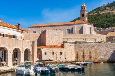 DUBROVNIK, CROATIA - 24 Haziran 2024: Ortaçağ simgeleriyle Eski Dubrovnik Limanı manzarası. Yüzlerce yıllık iskele duvarları ve kompakt bir limanın etrafını gözetleyenler lüks restoran teraslarıyla çevrili..