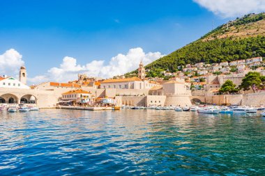 DUBROVNIK, CROATIA - 27 Haziran 2024: Ortaçağ simgeleriyle Eski Dubrovnik Limanı manzarası. Yüzlerce yıllık iskele duvarları ve kompakt bir limanın etrafını gözetleyenler lüks restoran teraslarıyla çevrili..