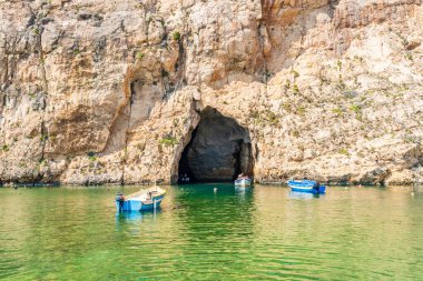 DWEJRA, GOZO, MALTA - SEPTEMBER 01.2024: Small boats take tourists through the sea tunnel to Azure window, a natural sea arch in Dwejra lagoon on the Gozo island. clipart