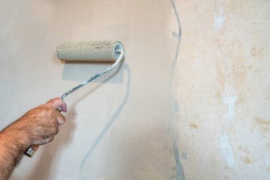 Duvarı boyayan bir boya silindiri ile dekoratörün eli - ev yenileme konsepti - seçici odak