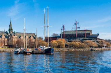 STOCKHOLM, SVEDEN - 08 Mart 2025: Stockholm takımadalarındaki Djurgarden adasında kıyıya demirlemiş yatlar ve botlar ve arka planda İskandinav müzesi
