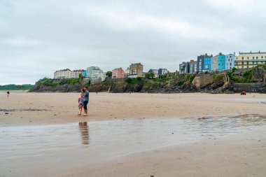 TENby, Wales - 28 Haziran 2021: insanlar güneybatı Galler 'de Tenby' de kumlu bir plaj boyunca yürürler. Tenby, 13. yüzyıl kasaba duvarları ve Castle Beach de dahil olmak üzere kumlu kıyı şeridi ile ünlüdür.