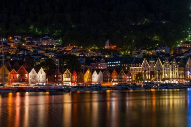 BERGEN, NORway - 16 AĞUSTOS 2025: Alacakaranlıktaki bir limanın karşısındaki ünlü Bergen Bryggen bölgesinin manzarası. Bryggen, 1979 yılından beri UNESCO 'nun Dünya Kültür Mirasları listesinde yer alıyor..