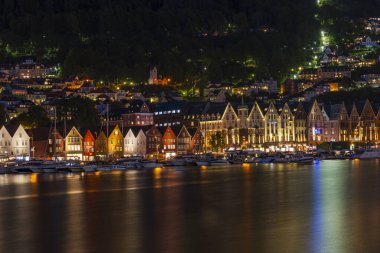 BERGEN, NORway - 16 AĞUSTOS 2025: Alacakaranlıktaki bir limanın karşısındaki ünlü Bergen Bryggen bölgesinin manzarası. Bryggen, 1979 yılından beri UNESCO 'nun Dünya Kültür Mirasları listesinde yer alıyor..