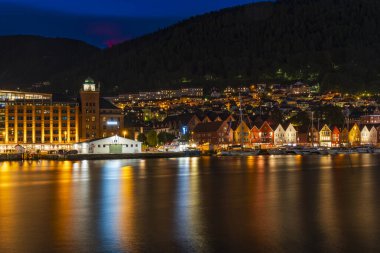 BERGEN, NORway - 16 AĞUSTOS 2025: Alacakaranlıktaki bir limanın karşısındaki ünlü Bergen Bryggen bölgesinin manzarası. Bryggen, 1979 yılından beri UNESCO 'nun Dünya Kültür Mirasları listesinde yer alıyor..