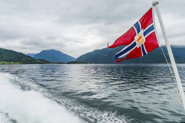 Arka planda fiyort manzaralı bir feribotta Norveç bayrağı