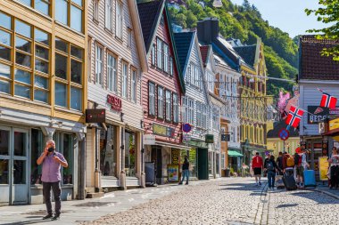 BERGEN, NORway - 15 AĞUSTOS 2025: Geleneksel renkli İskandinav binaları Norveç 'in Bergen kentindeki kaldırımlı bir cadde üzerindedir. Bergen Norveç 'in güneybatı kıyısında dağlar ve fiyortlarla çevrili bir şehirdir.