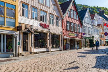 BERGEN, NORway - 15 AĞUSTOS 2025: Geleneksel renkli İskandinav binaları Norveç 'in Bergen kentindeki kaldırımlı bir cadde üzerindedir. Bergen Norveç 'in güneybatı kıyısında dağlar ve fiyortlarla çevrili bir şehirdir.