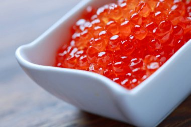 Red Caviar in bowl over wood background. Close-up salmon caviar