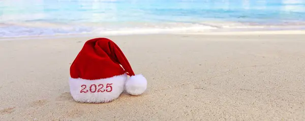白色的加勒比沙滩上挂着一顶快乐的圣诞帽 2025年新年背景 图库图片