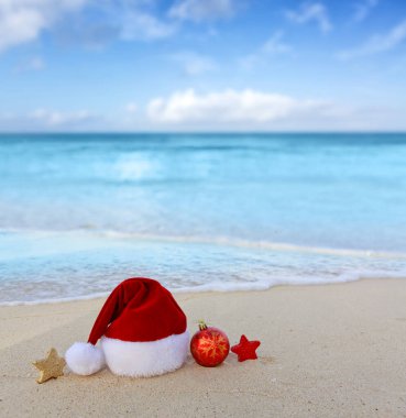 Beyaz Karayip kumları üzerindeki Noel Baba şapkası ve süslemeleri ile mutlu Noeller..