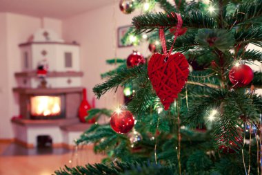 Kırmızı süslemeli ve şöminenin arka planında bulanıklık olan Noel ağacı dalı.