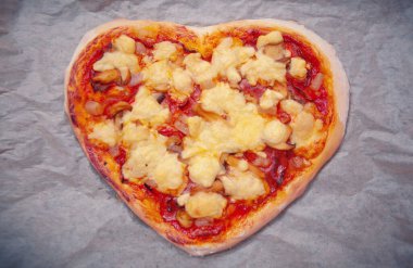 Gri arkaplanda domates soslu kalp şeklinde İtalyan pizzası..