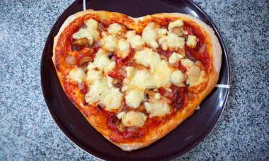 Gri arkaplanda domates soslu kalp şeklinde İtalyan pizzası..