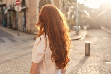 Sıcak yaz sabahında, kızıl kadının tuğladan yapılmış eski kasabanın tadını çıkarışının arka görüntüsü. Genç kız dışarıda tek başına yürüyor.