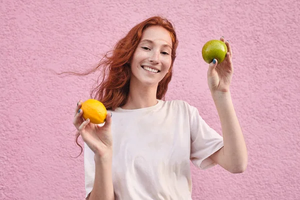 年轻的素食主义者 穿着休闲装 头戴苹果和橘子水果 头戴粉刷粉墙的背景 面带微笑 健康食品概念 — 图库照片