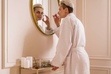 Aynanın önünde makyaj hazırlarken kirpiklerini kirpik bigudiyle şekillendiren özenli bir kadın. Stok fotoğrafı