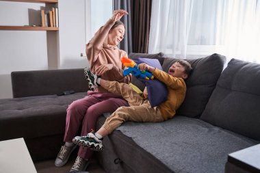 Aktif oyun. Genetik bozukluğu olan beyaz kadın ve çocuğunun evde oyuncak tabancayla oynamalarının geniş açılı görüntüsü. Stok fotoğrafı