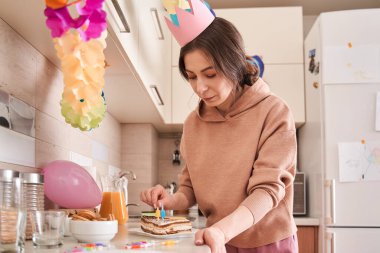 Doğum günü pastasını mumlarla süslerken mutfakta vakit geçiren konsantre kadının düşük açılı görüntüsü. Kutlamalar konsepti