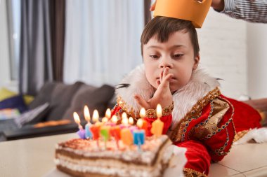 Down sendromlu şirin bir çocuk. Kral kostümü giyiyor. Evde doğum gününü kutlarken pastayı mumlarla seyrediyor.