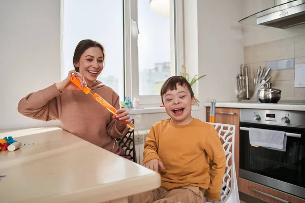 Im happy. Little boy with genetic disorder laughing out loud while his mother blowing soap bubbles with him at the kitchen. Stock photo